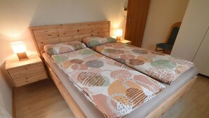 Een tweepersoonsbed met een beddengoed met dessin, een houten hoofdeinde, twee nachtkastjes met lampen, en een stoel in de hoek.