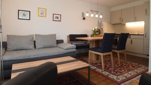 Een moderne woonkamer met een bank, een eettafel met stoelen, een keuken met kasten en een hanglamp.