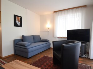 Un salón con un sofá, una televisión y una lámpara fijada a la pared.