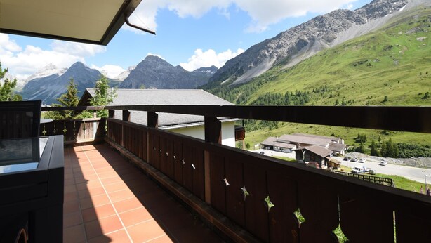 Een balkon met uitzicht op een berglandschap, een gebouw met een schuin dak en een heldere lucht.