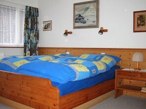 Ein hölzernes Bett mit einer blau-gelben Steude, ein Nachttisch mit einer Lampe und zwei Wandlampen.