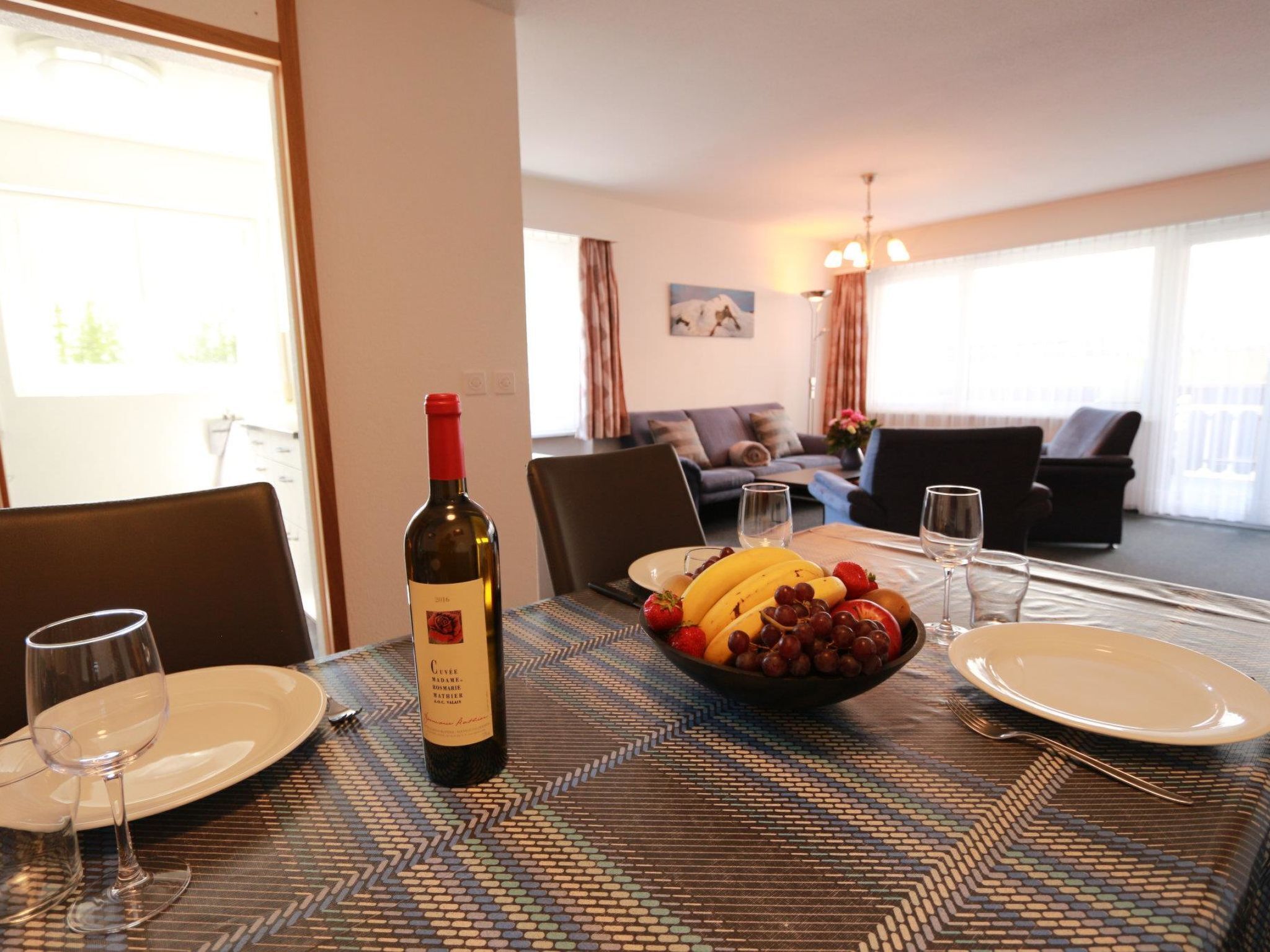 Una mesa de comedor con una botella de vino, un bol de fruta y platos y vasos.