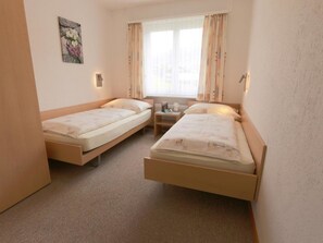 A hotel room with two single beds, a small bedside table with a lamp, a window with curtains, and a painting on the wall. - Azur Appartement/Fewo 4-Bettwohnung Nr. 2 by Interhome (Saas-Fee)