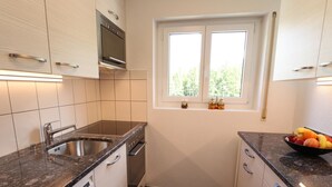 Ett kompakt kök med en diskho i rostfritt stål, en inbyggd ugn och ett fönster med utsikt över grönområden.