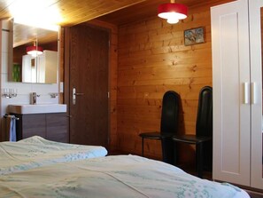 A room with wooden walls, a bed with a floral bedspread, a white wardrobe, a mirror, and a sink. - Weideli Appartement/Fewo 6 Bettwohnung Nr. 21 by Interhome (Saas-Grund)