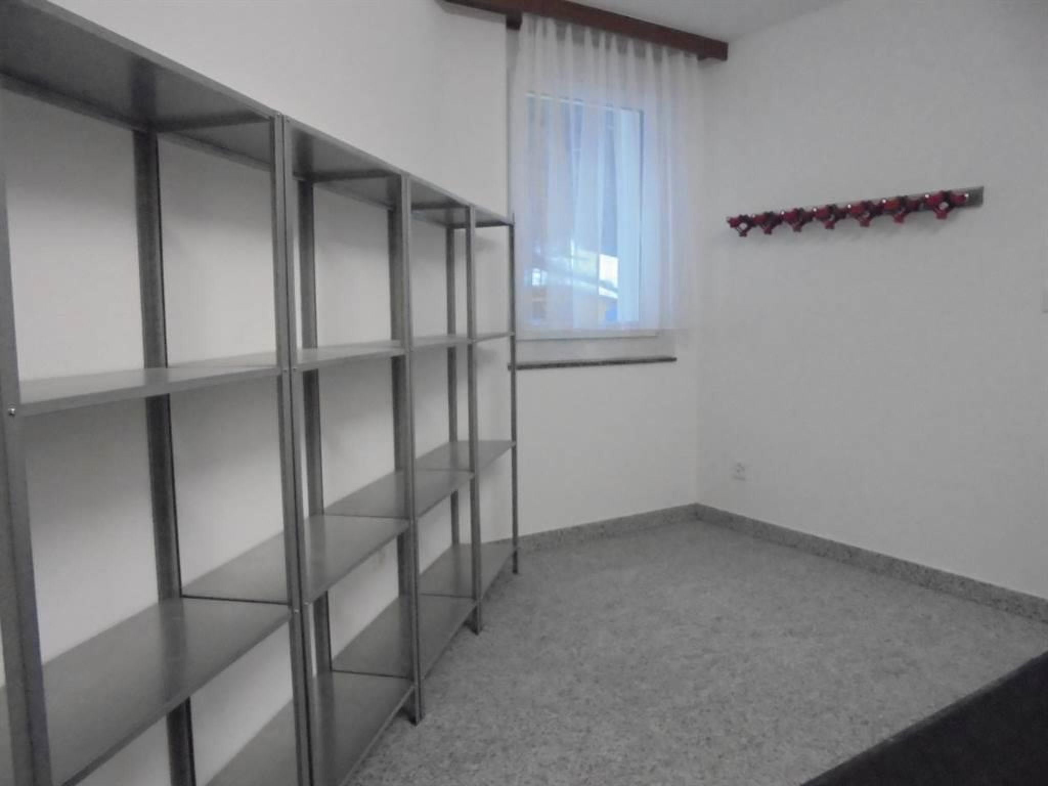 A room with a metal shelving unit, a window with white curtains, and a small decorative item on the wall.