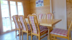 Ein Zimmer mit Holzwänden, einem Esstisch und sechs Stühlen, jeweils mit kariertem Sitzkissen.