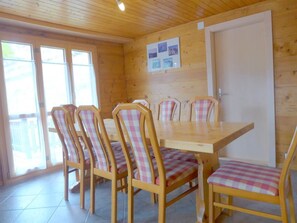 Een kamer met houten lambrisering, een eettafel en zes stoelen, elk voorzien van een geruit kussen.