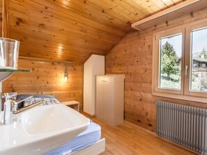 L’intérieur d’un chalet en bois comprend un lit, un lavabo, un placard et une fenêtre donnant sur un paysage verdoyant.