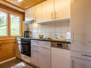 Uma cozinha compacta com fogão, forno, lava-louças e uma janela com vista para uma paisagem verde.