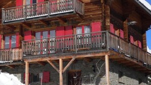 Eine Holzhütte mit Balkon und roten Fensterläden, umgeben von Schnee.
