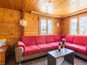 Ein Holzinnenraum mit einem roten Sofa, einem Tisch mit Flasche und Blumen sowie einem Poster an der Wand.