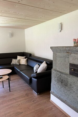 Een moderne woonkamer met een zwarte leren bank, een klein rond tafeltje en een stenen open haard.