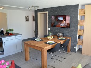 Ett modernt kök med en matplats, en TV som är monterad på väggen och ett träbord med stolar.