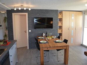 Un espace repas moderne avec une table en bois, des chaises et un téléviseur à écran plat fixé au mur.