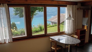 A room with a wooden table and chairs, a window with curtains, and a view of a lake and mountains. - Kaisers Ferienwohnung Appartement/Fewo 3-Bettwohnung by Interhome (Niederried)