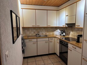 Une cuisine avec des meubles blancs, un plan de travail en bois, un évier, un grille-pain et une bouteille de vin.