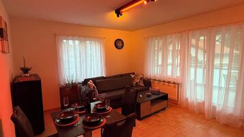 Ein Wohnzimmer mit einer Couch, einem Esstisch für zwei Personen und einer Uhr an der Wand.