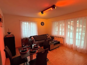A living room with a sofa, a dining table set for two, and a clock on the wall.