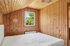 A bedroom with wooden walls, a window, a bed, and a ceiling fan.