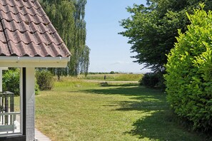 A covered outdoor area with a tiled roof, surrounded by greenery and a clear sky.