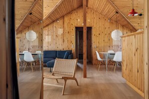 A wooden interior with a high ceiling, a dining area with chairs and a table, and a sofa. - Renovated, 4 rooms, sea view, beach, calm (Nysted)