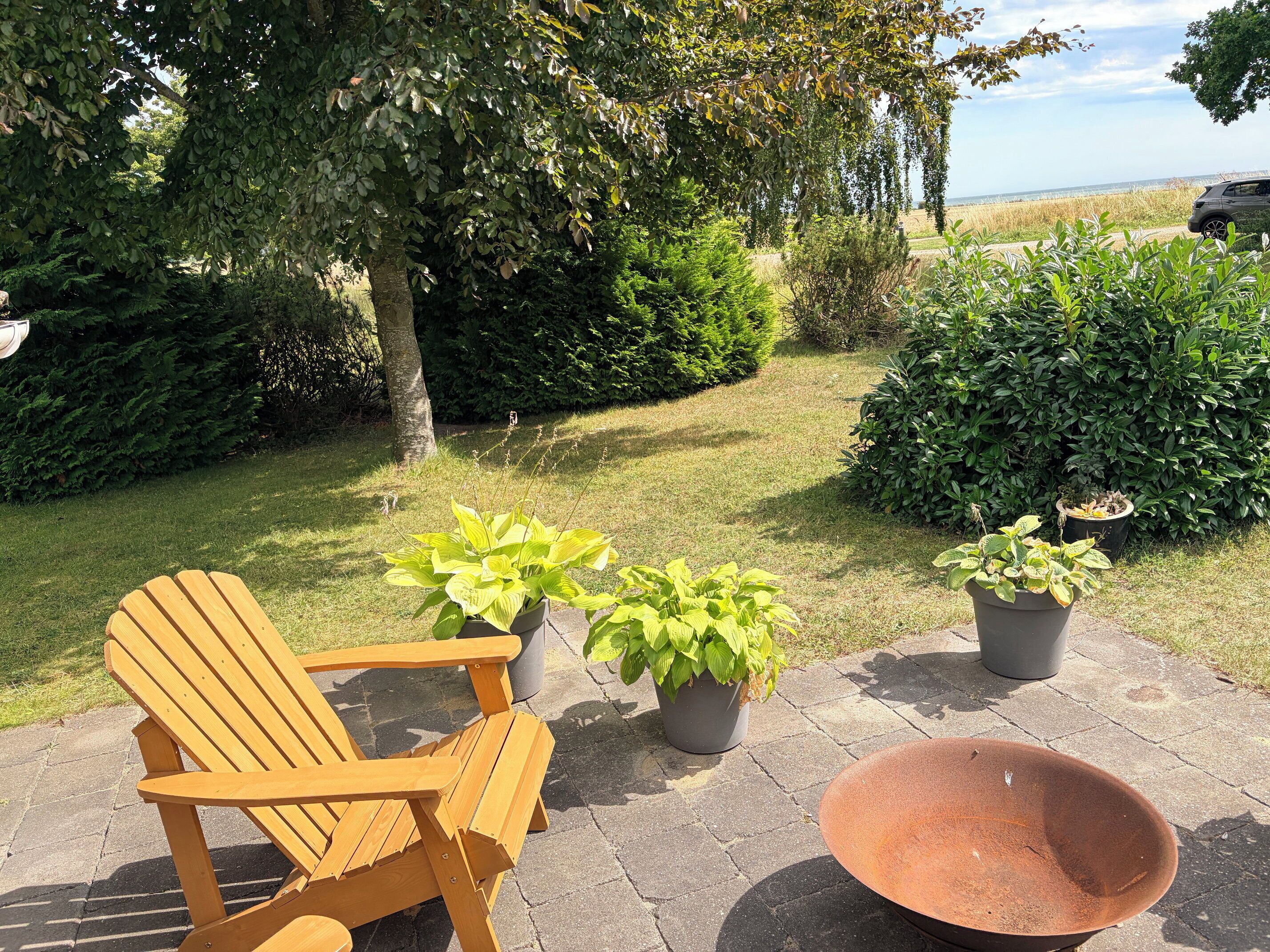 A wooden chair and potted plants on a patio with a view of the sea.