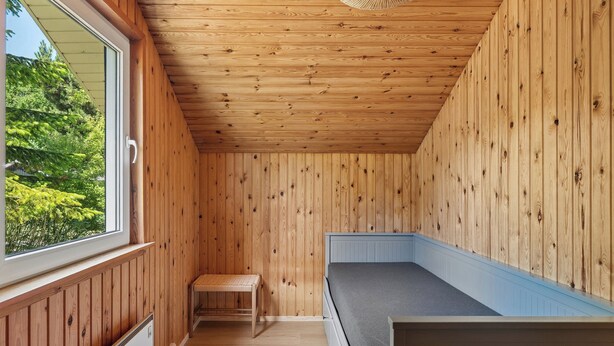 Een kamer met houten lambrisering, een bed, een bank en een raam.
