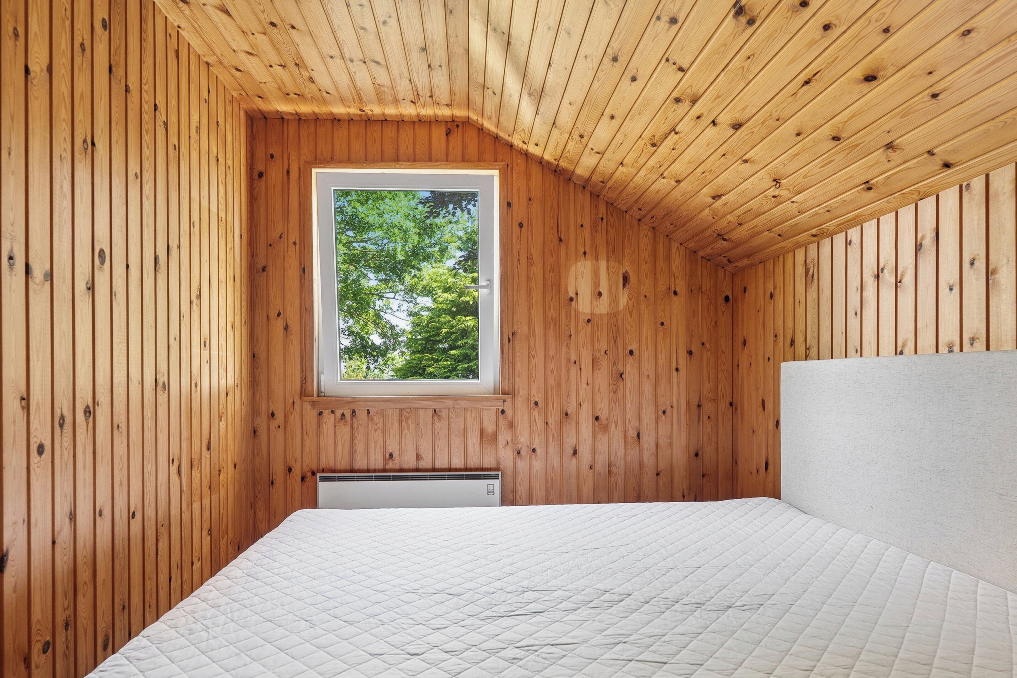 Une pièce aux murs en bois, avec une fenêtre, un lit et un radiateur.