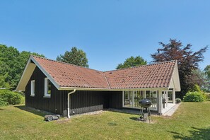A house with a sloped roof, a covered patio, and a barbecue grill in the yard.