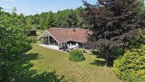 Een huis met een schuin dak, een overdekt terras met tuinmeubilair en een verzorgd gazon.