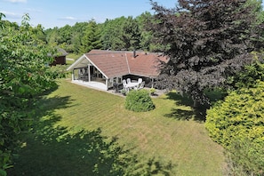 Une maison avec un toit en pente, un patio couvert aménagé avec du mobilier d’extérieur et une pelouse bien entretenue.