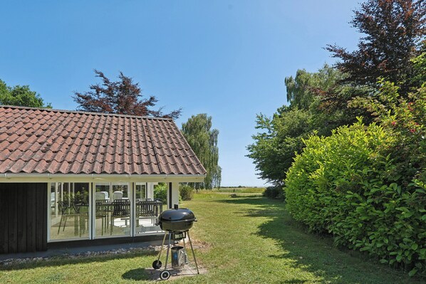 A house with a tiled roof, a covered patio with chairs, and a barbecue grill.