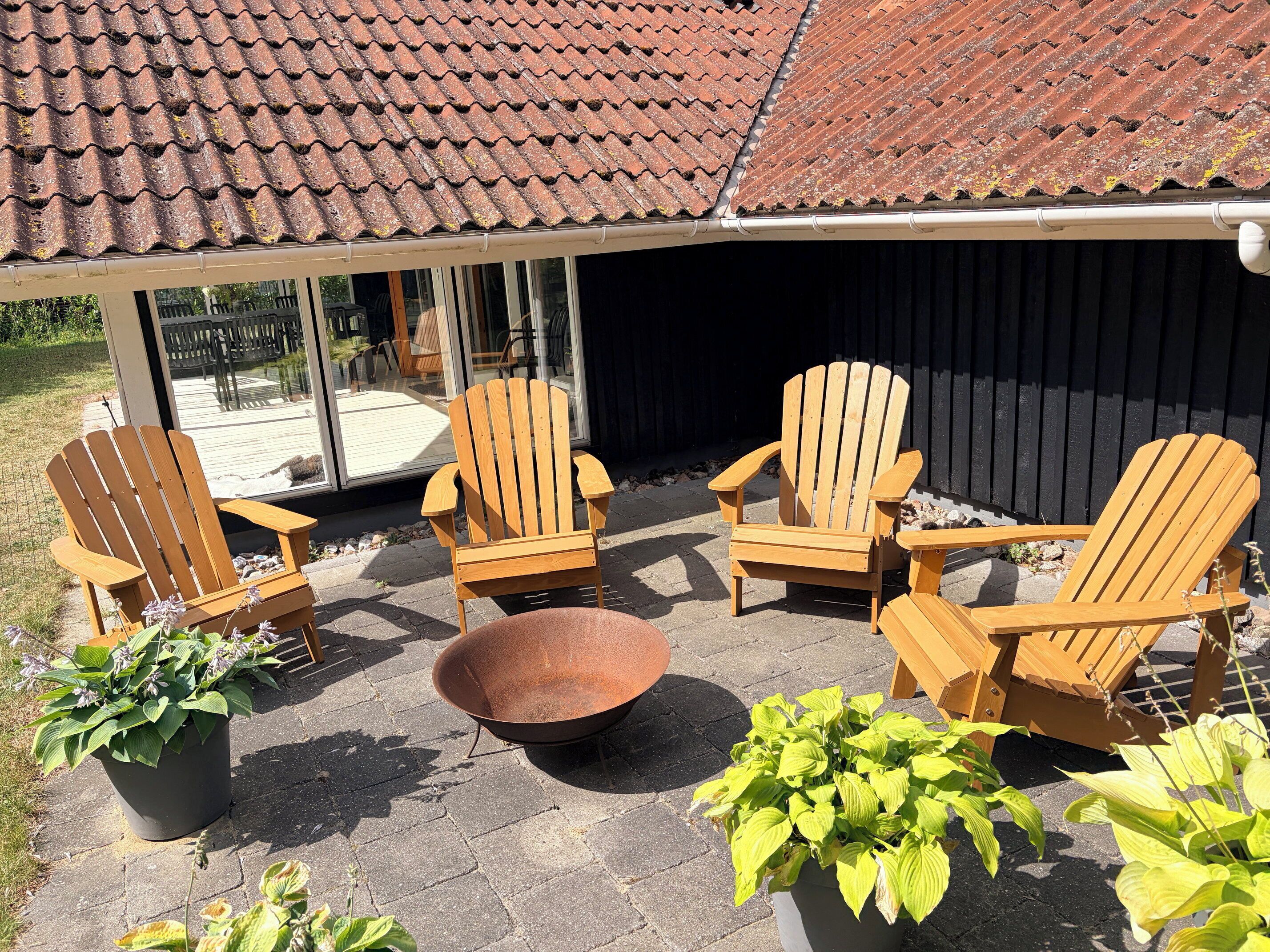 An outdoor seating area with wooden Adirondack chairs and a metal fire pit.