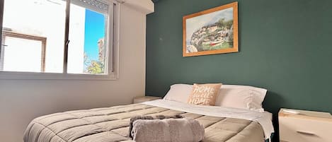 A bedroom with a bed, a window, a painting, and a nightstand.