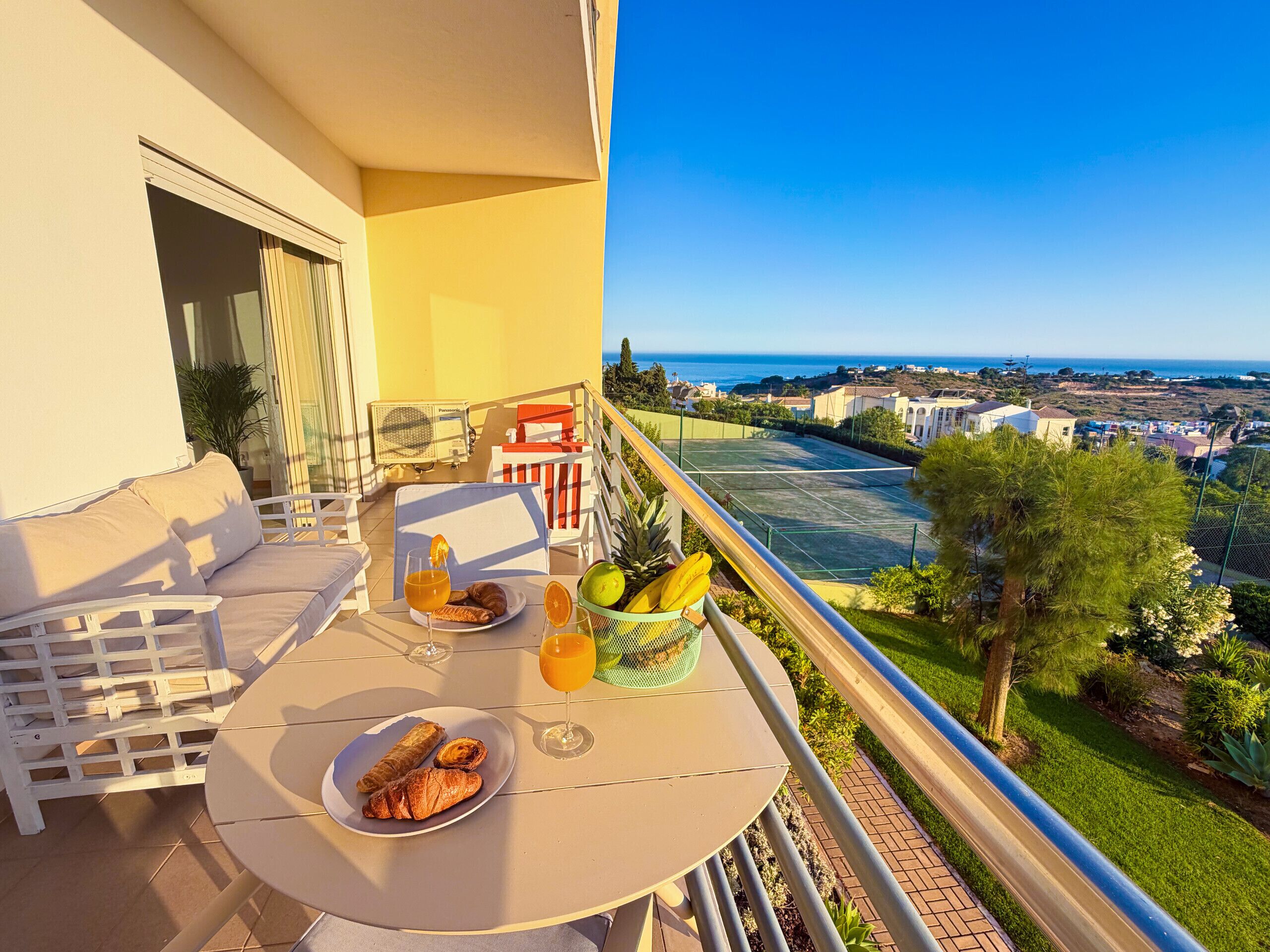 Un balcón con mobiliario exterior, una mesa con desayuno y vistas a la costa.