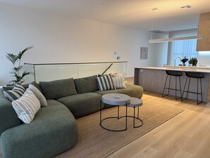 Een moderne woonkamer met een groene bank, gestreepte kussens, een kleine ronde tafel en een keuken met een barstoel.