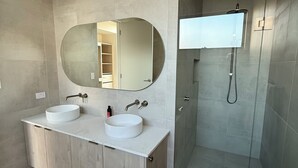 Ein modernes Badezimmer mit zwei Waschbecken, einem großen Spiegel und einer Duschkabine aus Glas.