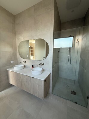 Ein modernes Badezimmer mit zwei Waschbecken, einem großen Spiegel und einer Duschkabine aus Glas.
