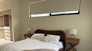 Ein Schlafzimmer mit einem Bett, zwei Nachttischen mit Lampen, einem Kleiderschrank und einem großen Fenster.