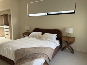 Ein Schlafzimmer mit einem Bett, zwei Nachttischen mit Lampen, einem Kleiderschrank und einem großen Fenster.
