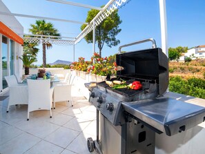 Eine Terrasse im Freien mit einem Grill, Korbstühlen, einem Tisch mit Geschirr und Blick auf die Landschaft.