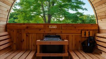 A sauna with wooden walls, a bench, a table with a grill, and a view of trees.