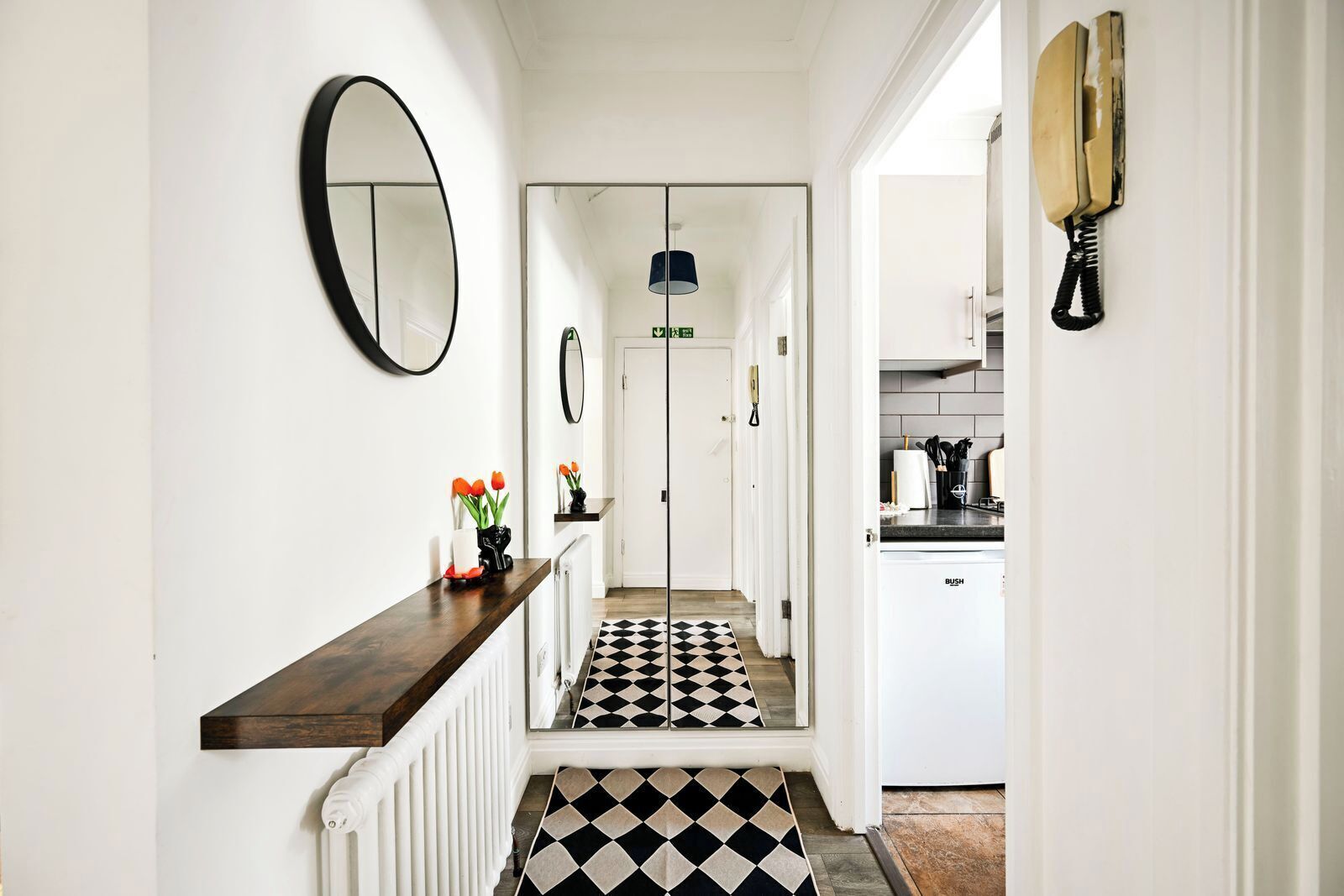 A hallway with a black and white checkered floor, a mirror on the wall, and a telephone on the right.