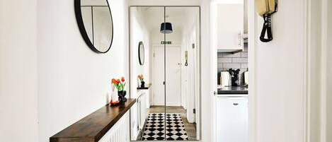 A hallway with a black and white checkered floor, a mirror on the wall, and a telephone on the right.