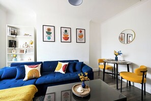 Ein modernes Wohnzimmer mit einem blauen Sofa, gelben Sesseln, einem Couchtisch und einem Bücherregal mit Dekoration.
