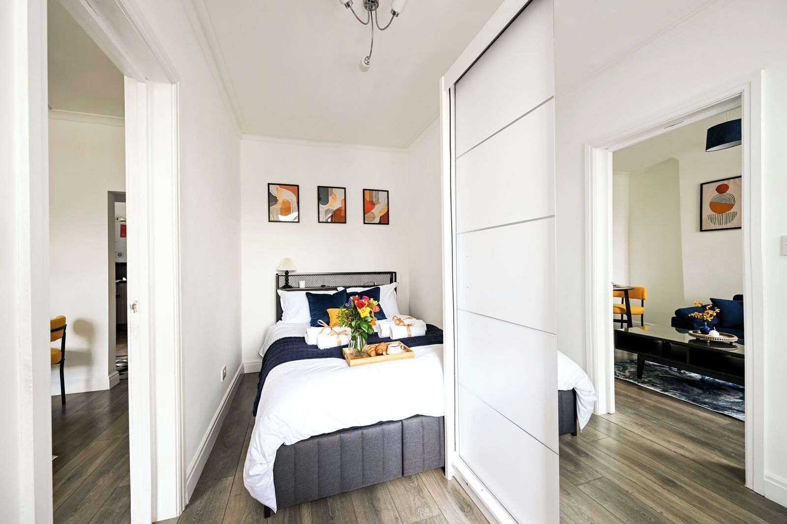 A hotel room with a bed, a bedside table, a mirror, and a view of the hallway.