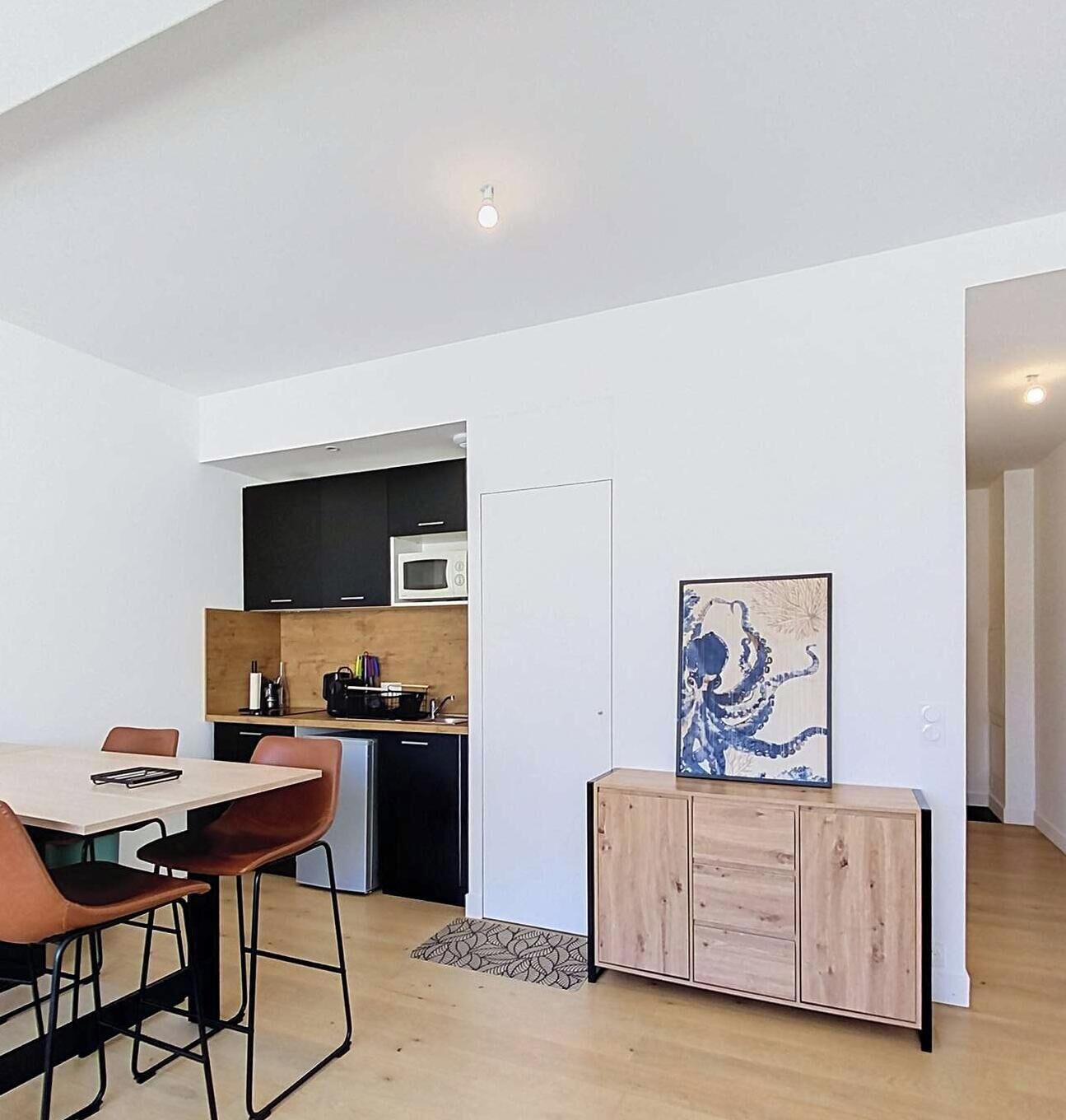 A modern kitchen with a microwave, a dining area with a table and chairs, and a cabinet with a painting.