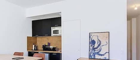 A modern kitchen with a microwave, a dining area with a table and chairs, and a cabinet with a painting.