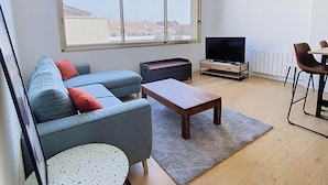 A modern living room with a sofa, a coffee table, a TV, and a dining area. - Holiday studio close to the ocean – Ideal for 2 people (LACANAU OCEAN)